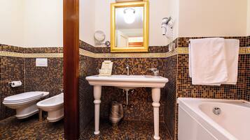 A bathroom with a white sink, two toilets, a bathtub, and a mirror with a gold frame.