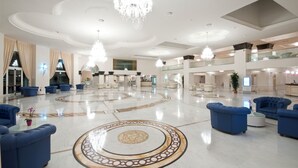 A spacious lobby with a central circular patterned floor, blue upholstered seating, chandeliers, and a modern ceiling design. - Grand Hotel Italia (Cluj-Napoca)