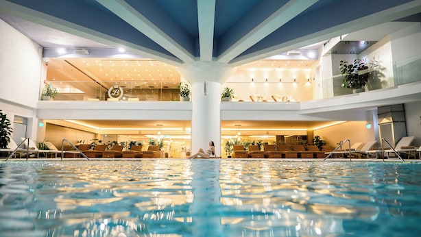 An indoor swimming pool with a central column, lounge chairs, and potted plants. - Grand Hotel Italia (Cluj-Napoca)