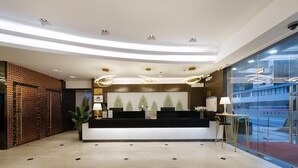 A modern reception area with a black counter, potted plants, and a glass wall with a view. - Wings Hotel Guangzhou (Foshan)