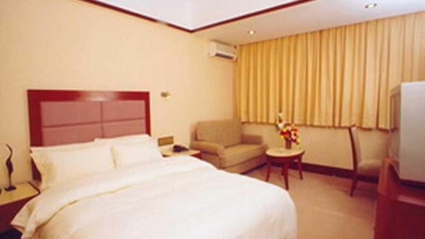 A hotel room with a bed, a chair, a small table with a vase, and a television. - Wings Hotel Guangzhou (Foshan)