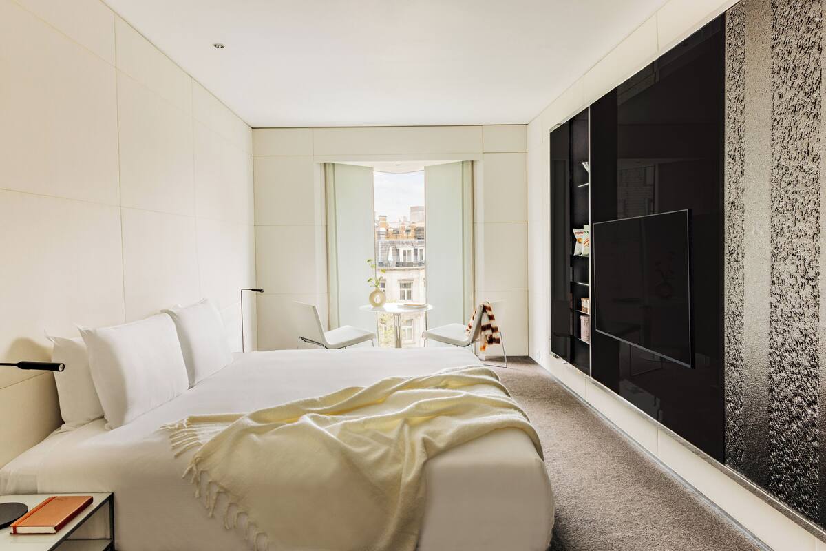 A modern hotel room with a large bed, a TV, and a view of the city.