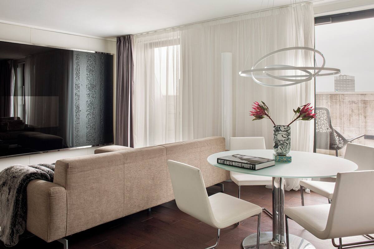 A modern living room with a sofa, chairs, a glass table, and a vase with flowers.