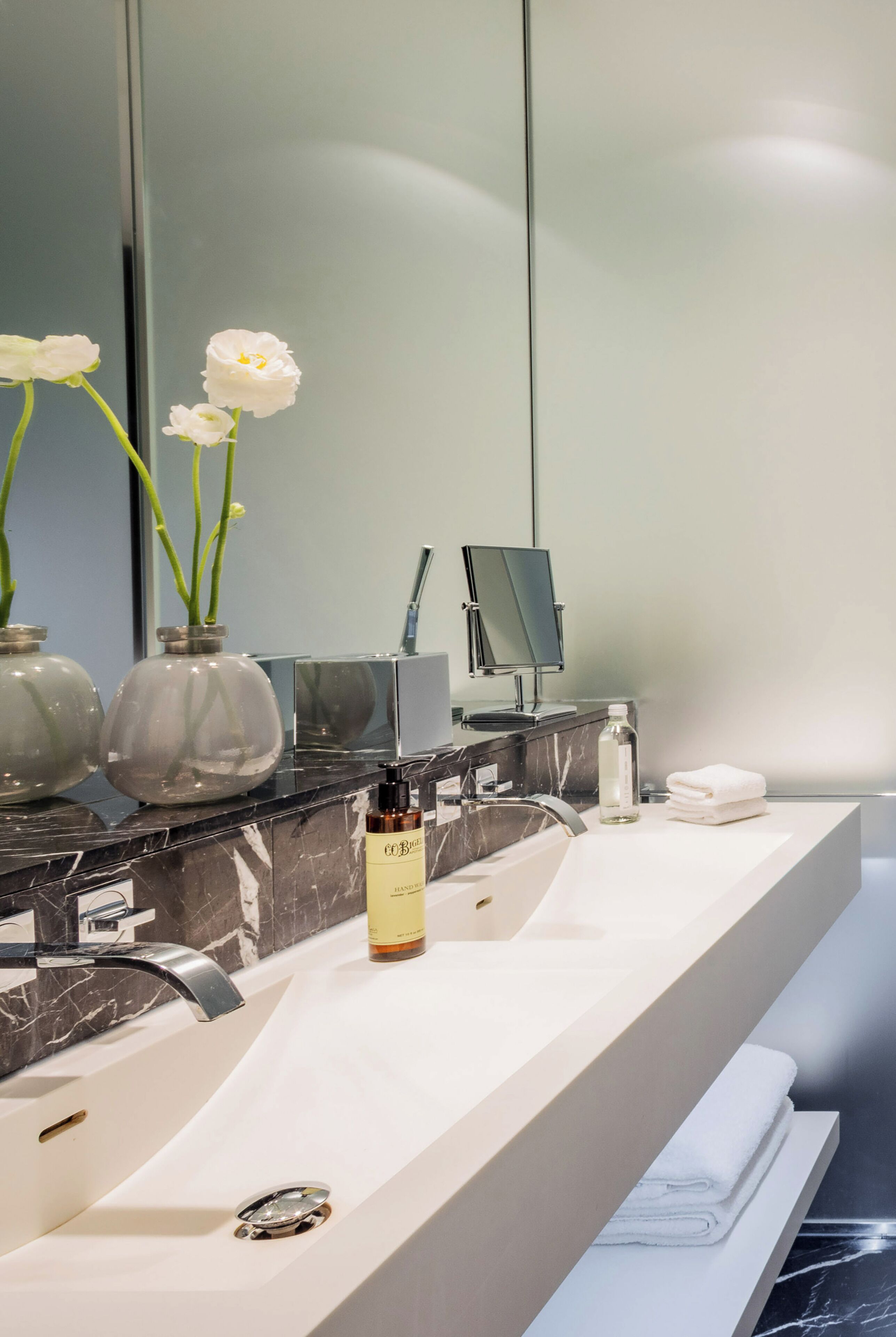 A modern bathroom with a marble sink, a mirror, and two glass vases with white flowers.