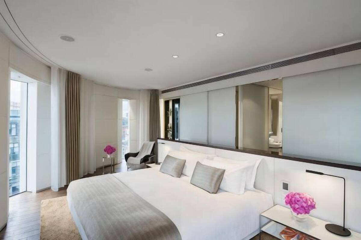 A modern hotel room with a large bed, a sitting area, a desk, and a large window.