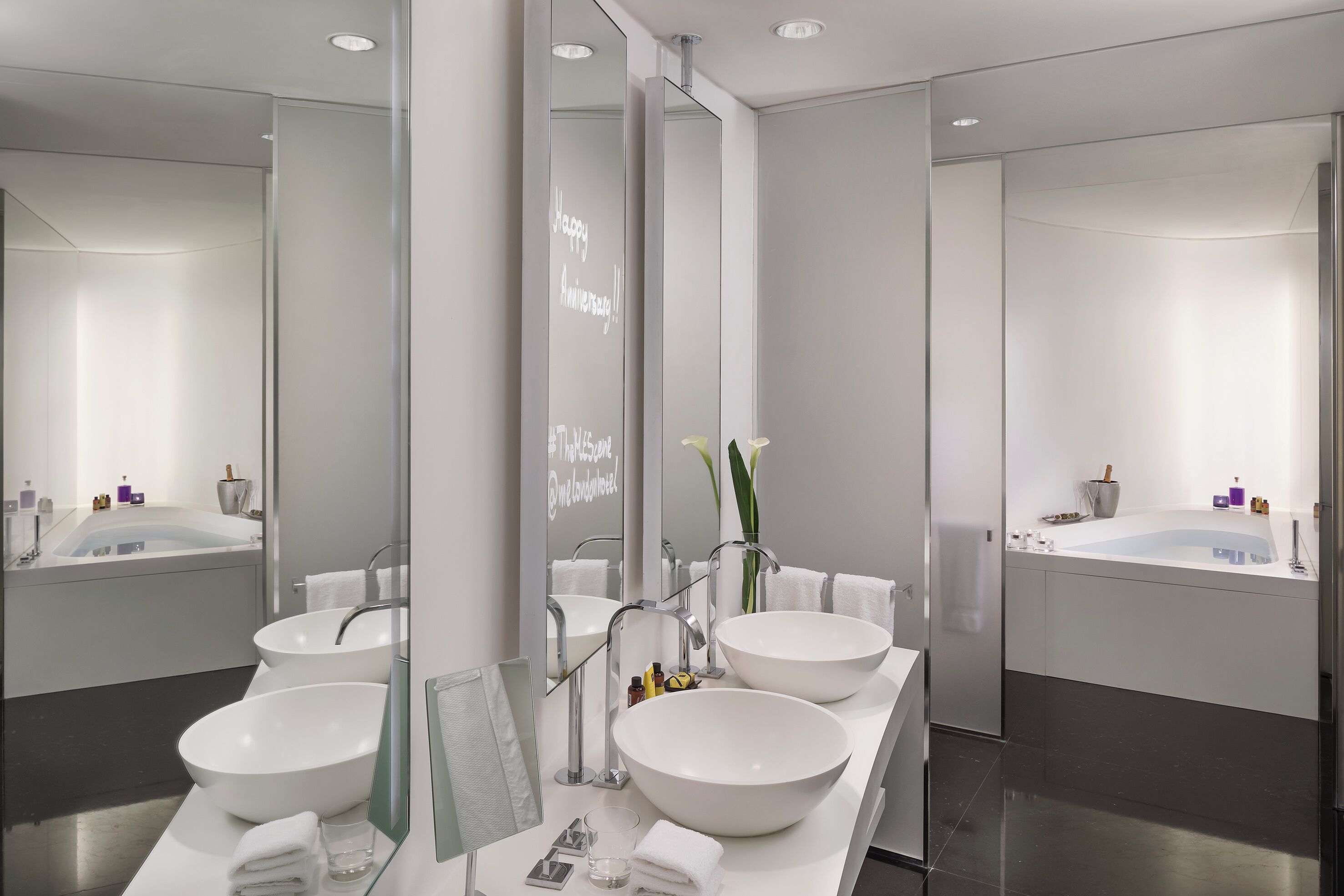 A modern bathroom with two large white sinks, a large mirror, and a bathtub.