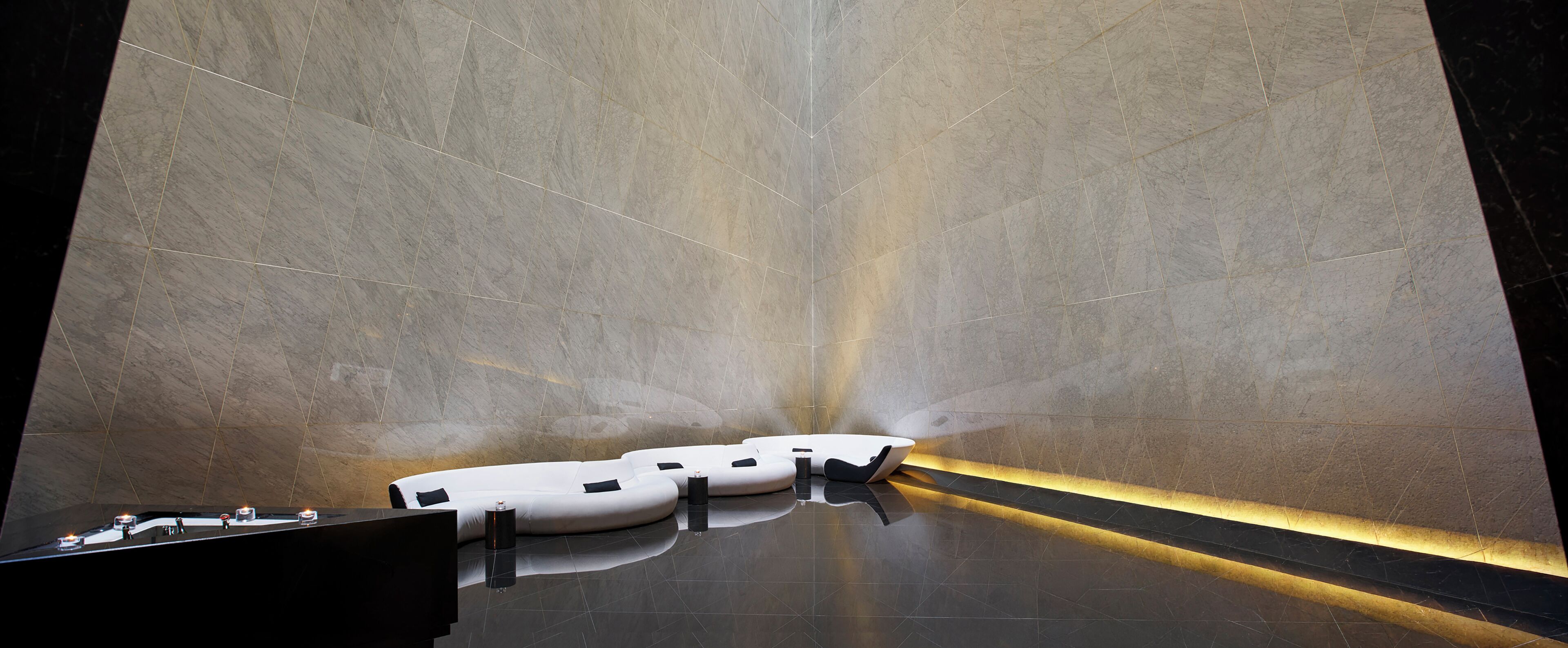 A modern bathroom with a reflective floor, a white bathtub, and a black countertop with a sink.
