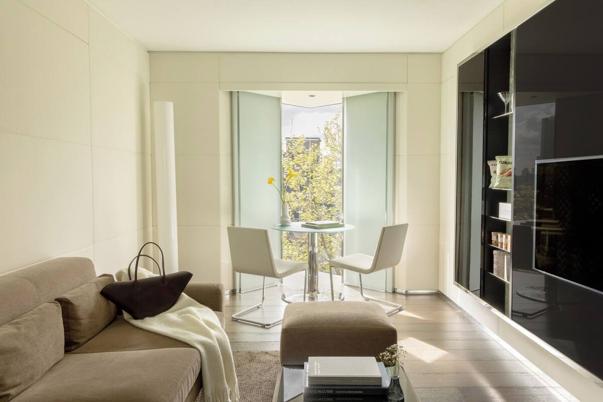 A modern living room with a sofa, a glass table with chairs, and a large window with a view of trees.