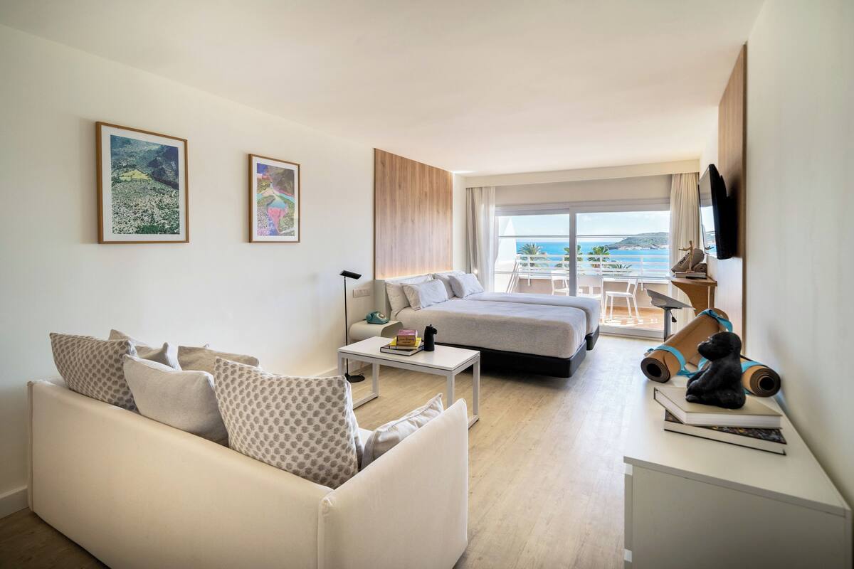 Habitación de hotel moderna con sofá, cama, una mesita y balcón con vista al mar.