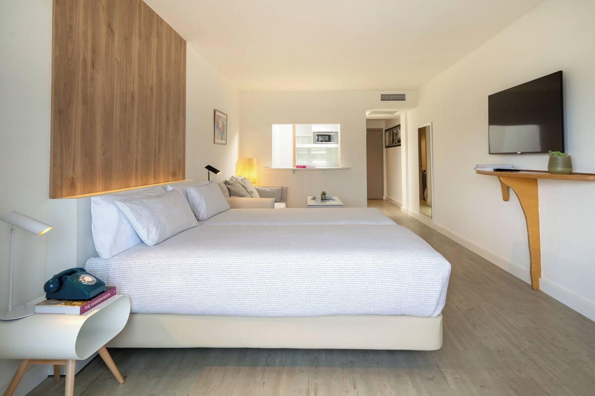 Un dormitorio moderno con una cama grande, una mesita de noche, una lámpara y un televisor sobre un soporte de madera.