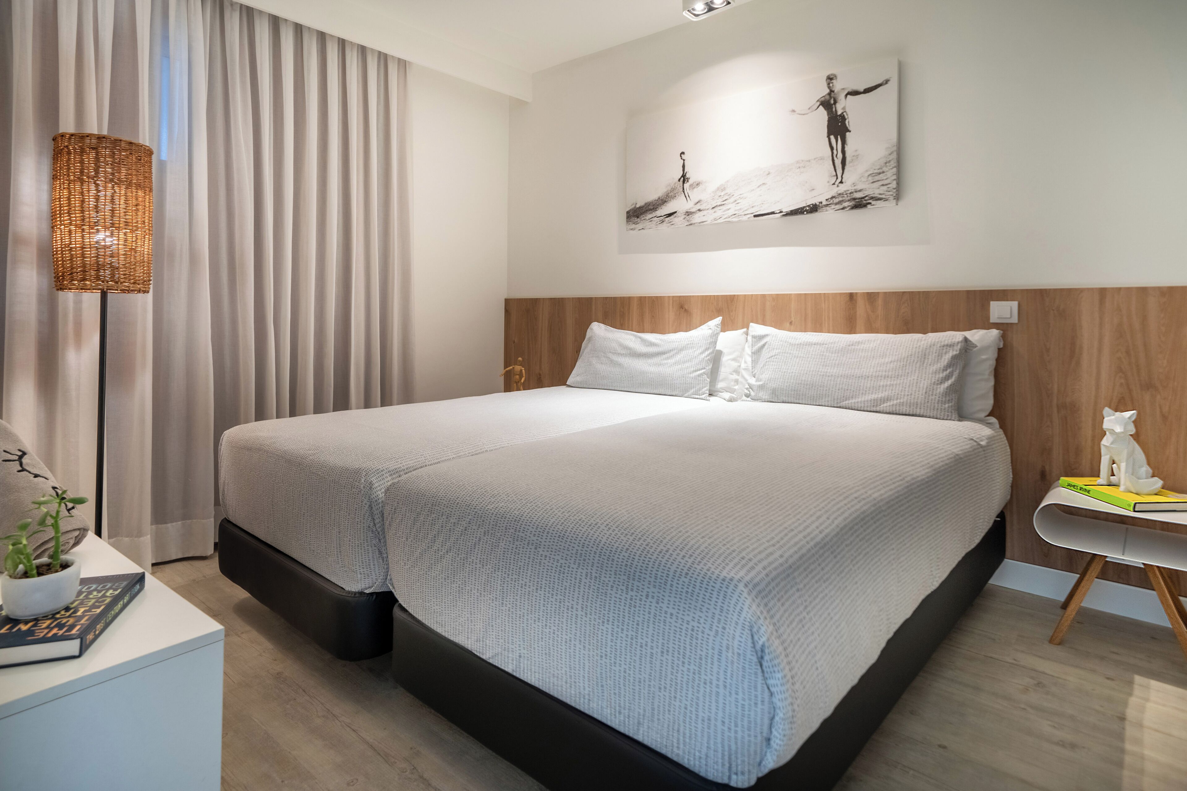 Una habitación de hotel moderna con una cama grande, una mesita de noche con una lámpara, una obra de arte colgada en la pared y una pequeña mesa con una figurita de gato.