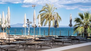 A beachside lounge with sun loungers and umbrellas, overlooking the sea and palm trees.