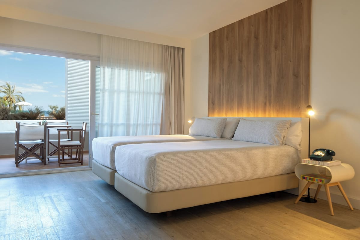 Un dormitorio moderno con una cama grande, un cabecero de madera, una mesita de noche con lámpara y vistas al exterior a través de una puerta corrediza.