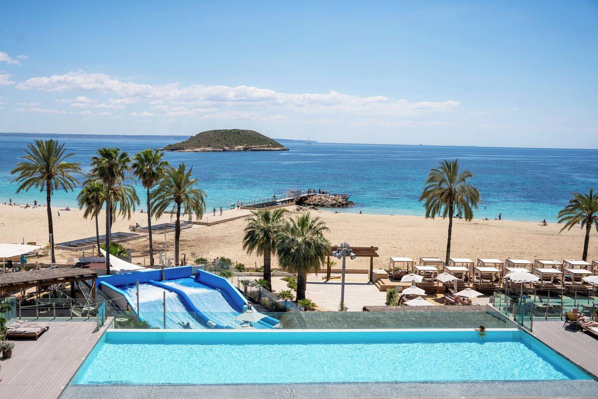 Zona de piscina con tobogán de agua, sillones de descanso y vista a la playa.