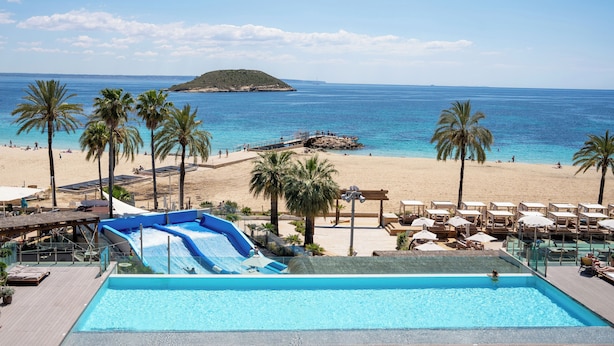 A pool area with a water slide, lounge chairs, and a beach view.