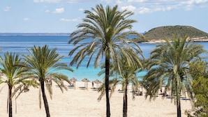 A beach with palm trees, clear blue water, and a distant hill.