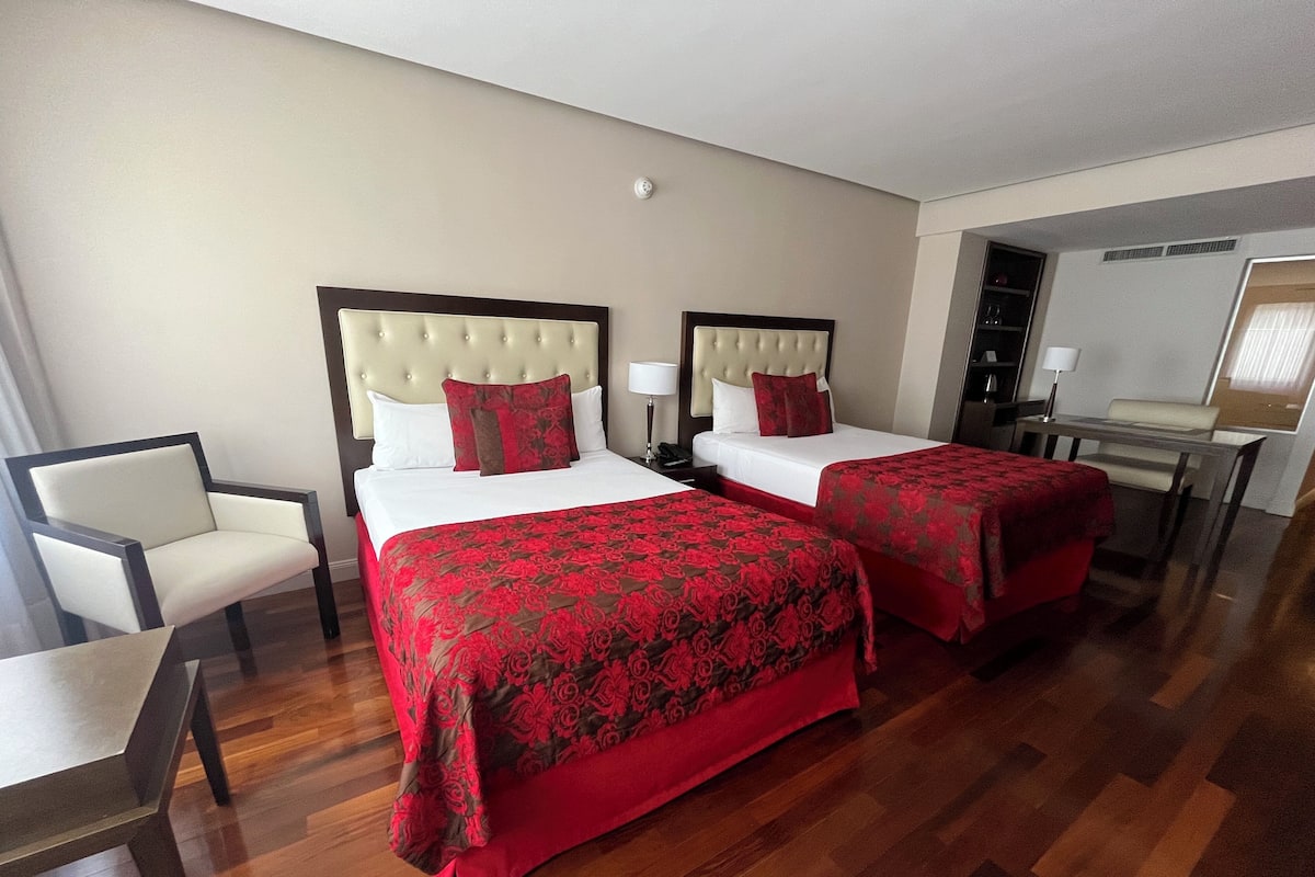Una habitación de hotel con dos camas, una silla, un escritorio y un espejo.