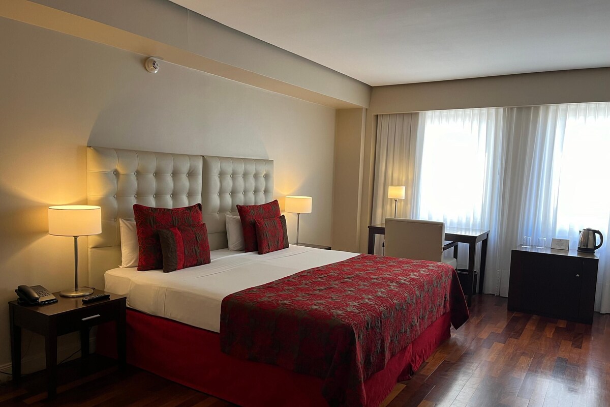 Une chambre d’hôtel avec un grand lit, deux lampes de chevet, un bureau, une chaise et une vue sur l’extérieur par la fenêtre.