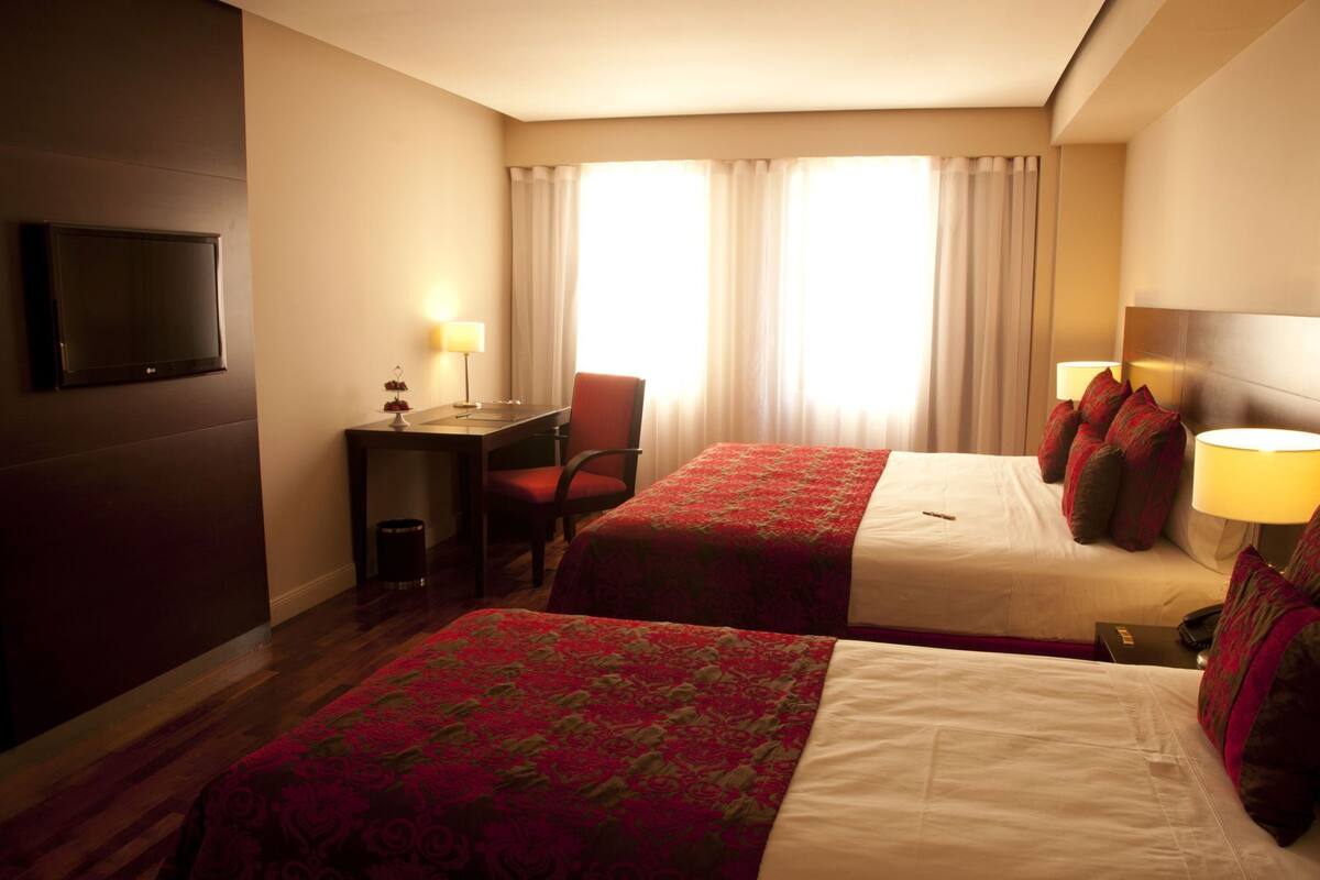 Habitación de hotel con dos camas, un escritorio, una silla, un televisor y una ventana con cortinas.