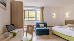 A hotel room with a bed, a desk with a laptop, a chair, and a window with curtains. - Lagrange Apart'HOTEL L'Escale Marine (La Rochelle)