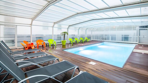A covered swimming pool area with lounge chairs and a wooden deck. - Lagrange Apart'HOTEL L'Escale Marine (La Rochelle)