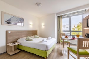 Habitación de hotel con cama, mesita de noche, escritorio con silla, ventana con cortinas y televisor.