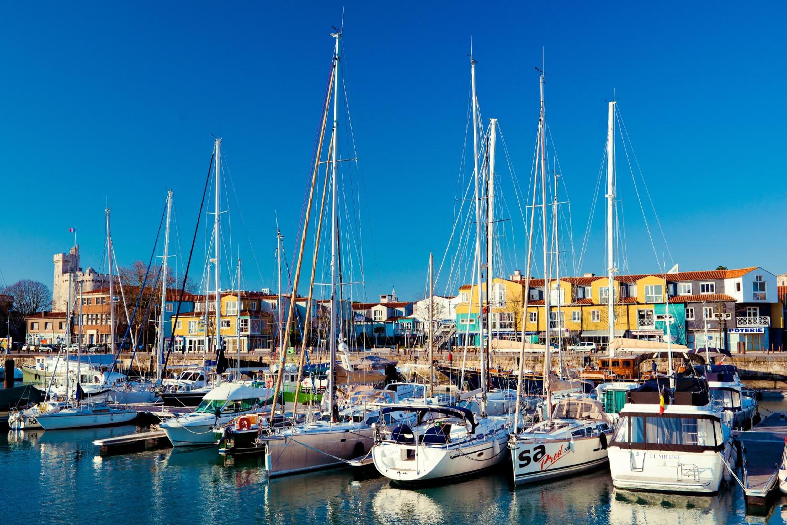 Un port de plaisance où sont amarrés de nombreux voiliers, entouré de bâtiments aux couleurs vives.