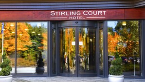 L’entrée de l’hôtel Stirling Court, avec une porte en verre, des plantes en pot et, en arrière-plan, le feuillage automnal.