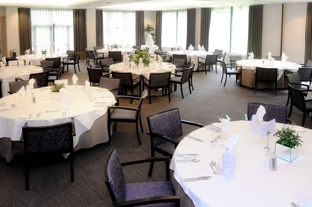 A hotel dining area with round tables set for dining, surrounded by chairs.