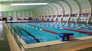 An indoor swimming pool with multiple lanes, a diving platform, and a seating area with numbered chairs. - Stirling Court Hotel (Stirling)