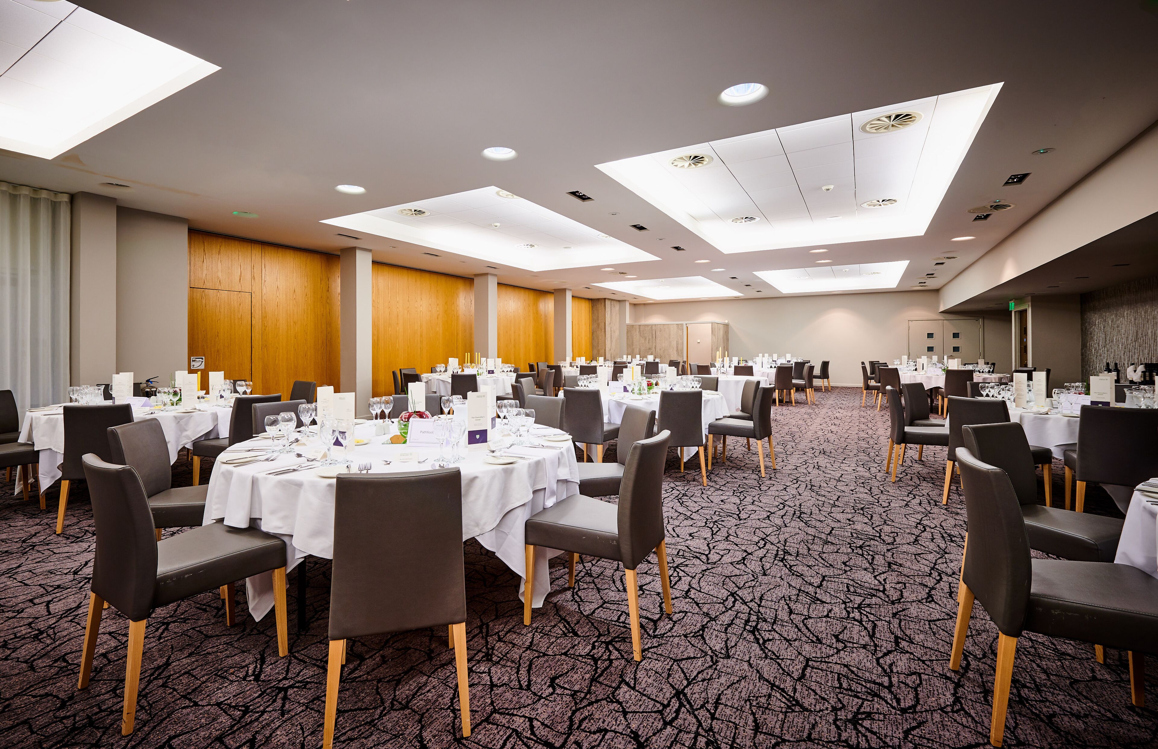 A large conference room with multiple round tables set for dining, equipped with chairs and table settings.