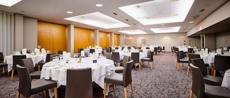 Un amplio salón de conferencias con varias mesas redondas dispuestas para comedor, equipado con sillas y vajilla.