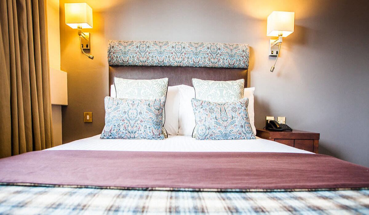 Habitación de hotel con una cama grande, dos lámparas de pared, una mesita de noche y un teléfono.