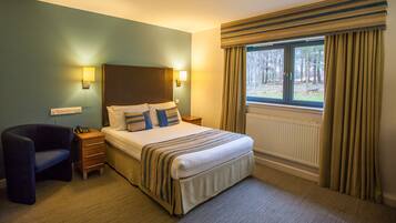 Een hotelkamer met een bed, bedlampjes, een stoel en een raam met gordijnen.