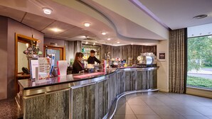 Un espace d’accueil d’hôtel doté d’un comptoir incurvé, d’un bar et offrant une vue sur l’extérieur grâce à de grandes fenêtres.