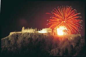 A historic building with a large, illuminated structure on a hill, surrounded by sparse vegetation. - Stirling Court Hotel (Stirling)