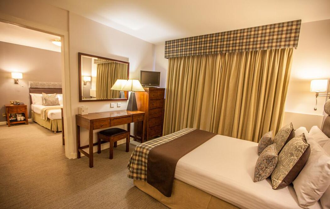 A hotel room with a bed, a desk, a chair, a television, and a large window with curtains.