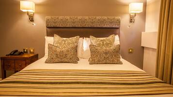 Habitación de hotel con una cama grande, cabecera estampada, dos lámparas de noche y un teléfono sobre una mesita de madera.