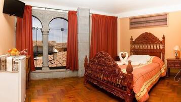Ein Schlafzimmer mit einem hölzernen Bett, einem Fernseher, einer Obstschale und Blick durch ein Fenster mit roten Vorhängen.