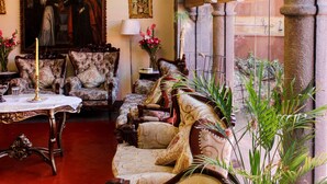 A room with a chandelier, floral armchairs, a large painting, and a view through an arched window. - Fuente de Agua Cusco Hotel (Cusco)