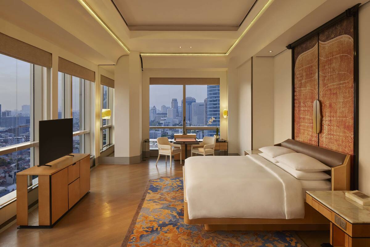 Ein modernes Hotelzimmer mit einem großen Bett, einem Schreibtisch und einem Fernseher. Es verfügt über große Fenster mit Blick auf die Stadt.