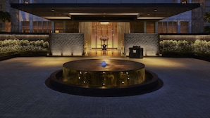 Un edificio moderno con una fontana circolare di fronte, un'area reception con un lampadario e una facciata in pietra.