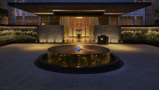 A modern building with a circular water feature in front, a reception area with a chandelier, and a stone facade. - Keraton at The Plaza, The Unbound Collection by Hyatt (Jakarta)