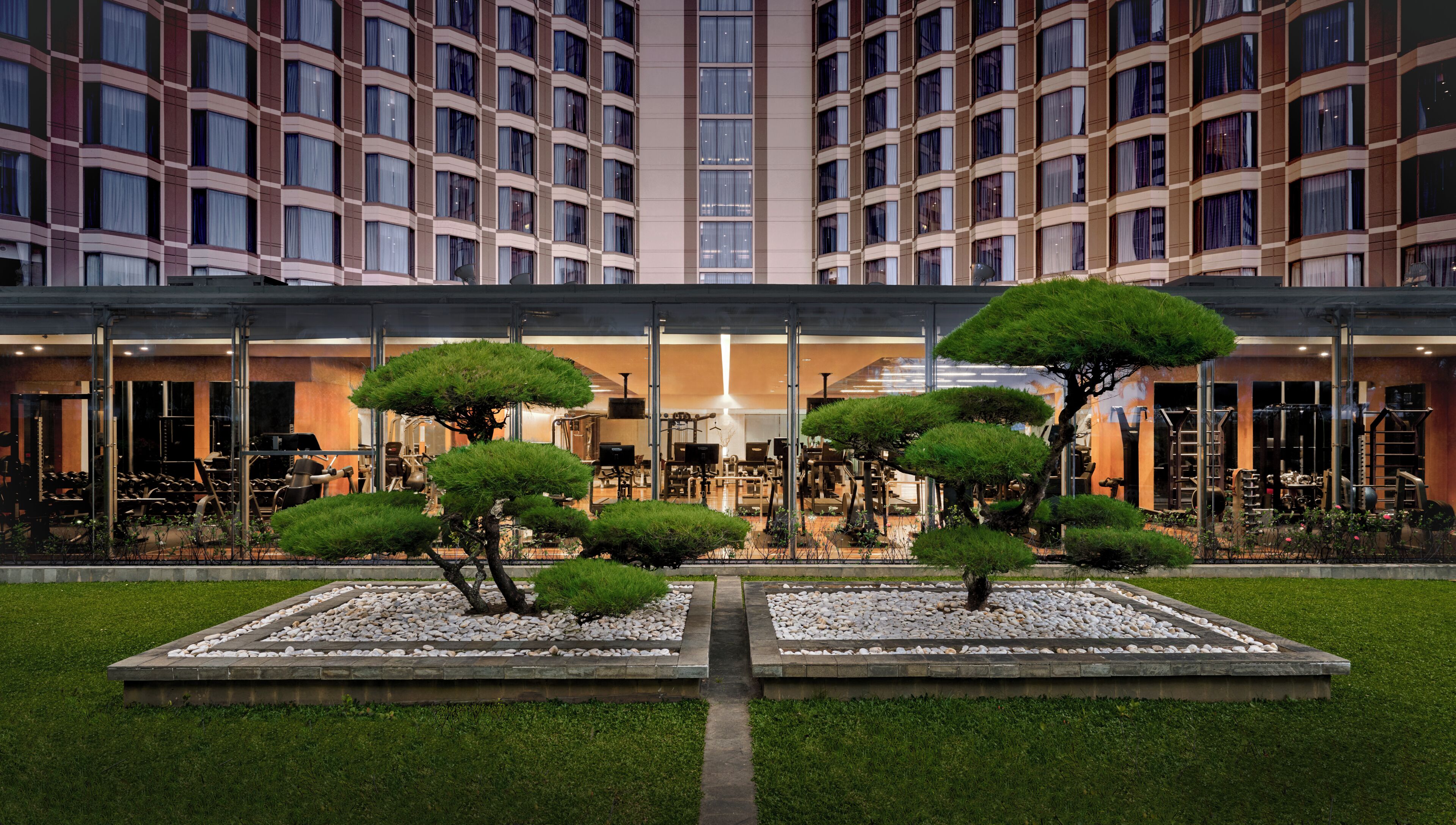 A hotel with a modern facade, a gym, and a well-maintained garden with trimmed bushes.
