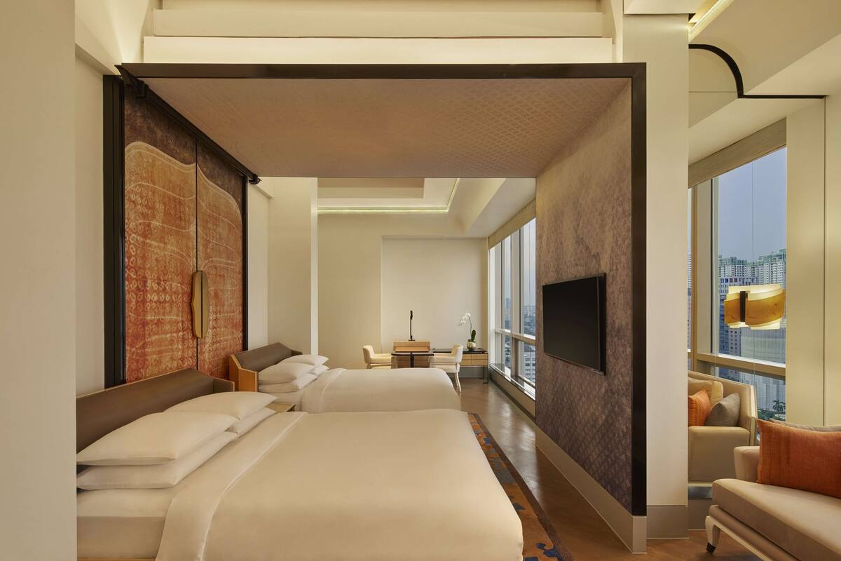 Ein modernes Hotelzimmer mit zwei Betten, einem Schreibtisch, einem Stuhl, einem Fernseher und einem großen Fenster mit Blick auf die Stadt.