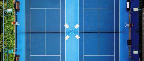 An aerial view of a tennis court with four service boxes, a net, and surrounding seating areas.