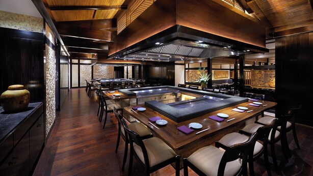 Un restaurante con una larga mesa compartida, techos altos y un diseño moderno.