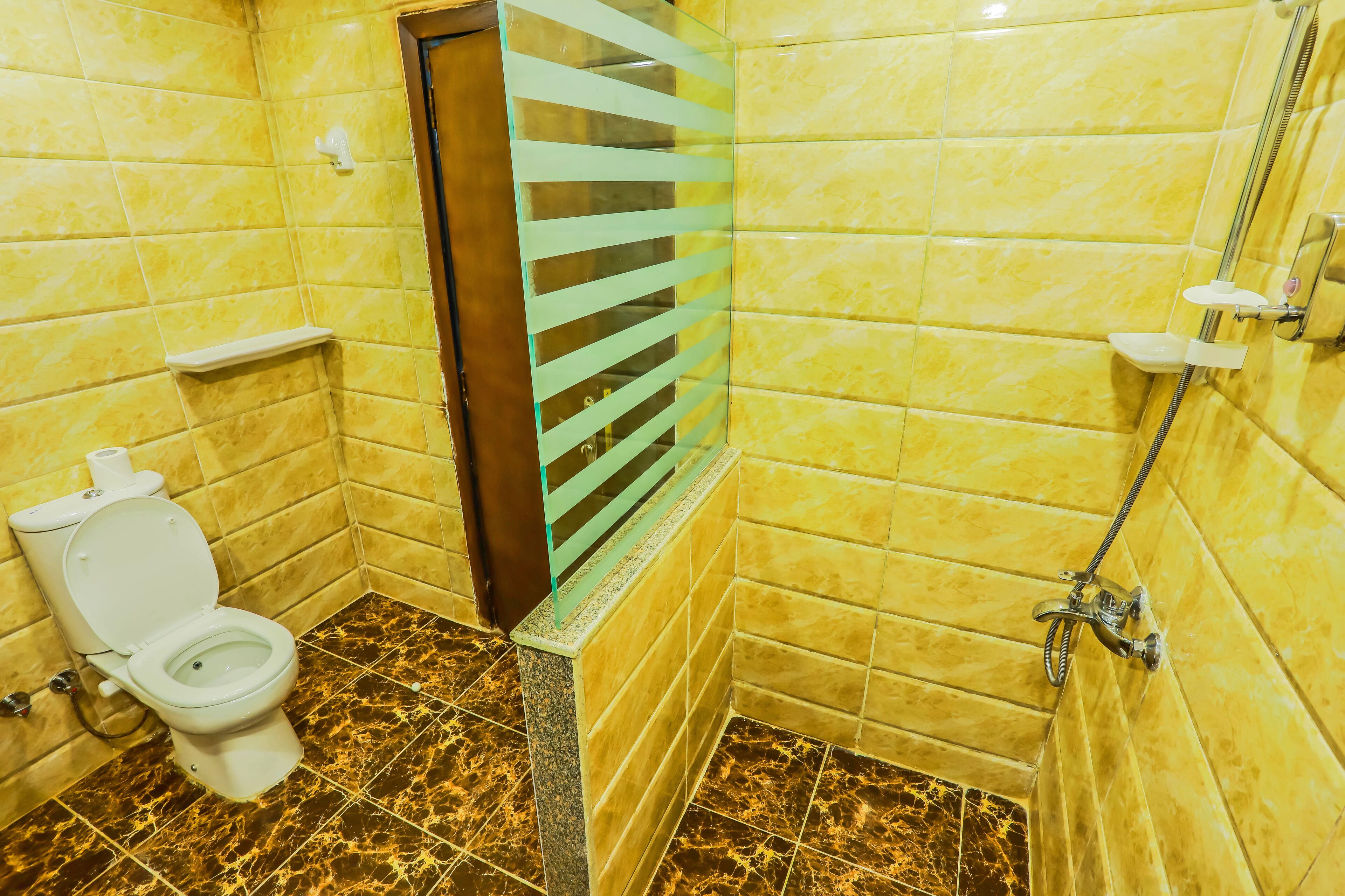 Un baño con paredes de azulejos amarillos, suelo de mármol, un inodoro, una ducha y un separador de vidrio.