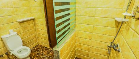 Un baño con paredes de azulejos amarillos, suelo de mármol, un inodoro, una ducha y un separador de vidrio.