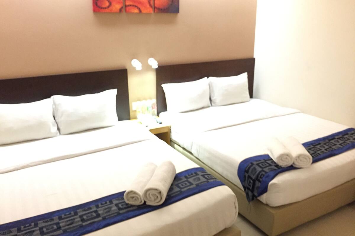 Two twin beds with white linens and blue patterned bedspreads, a nightstand with a lamp, and a red abstract painting on the wall.